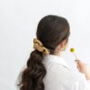 Rear view of a woman with wavy brown hair holding a small yellow flower in a minimalistic setting.